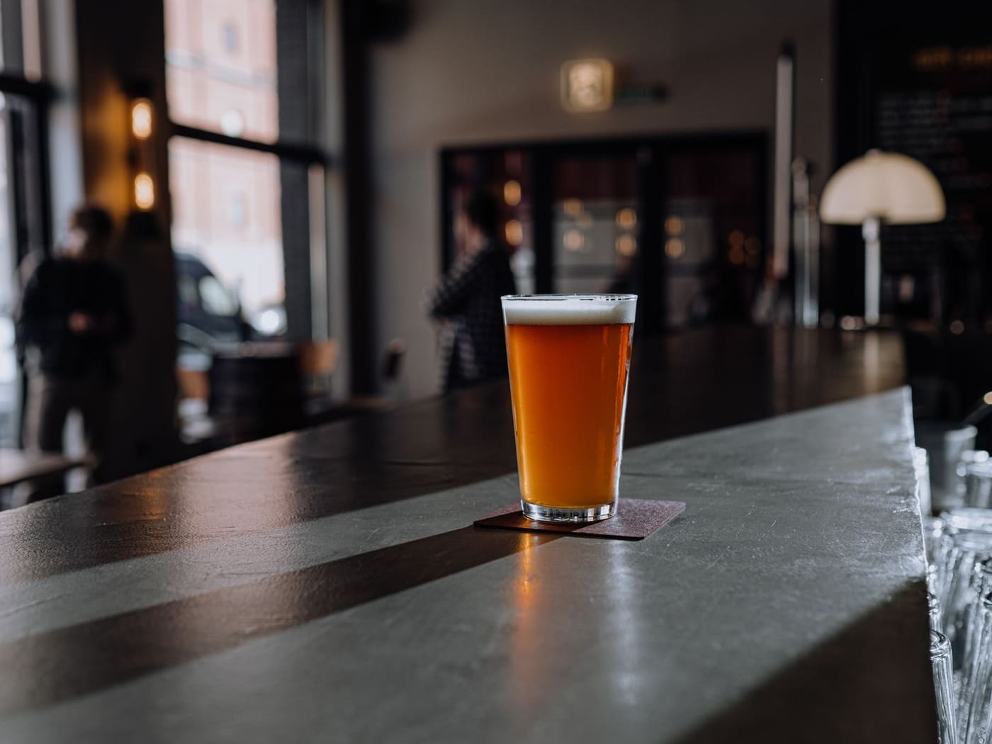 Vaso de cerveza servido sobre el mesón de un bar iluminado por la ventana